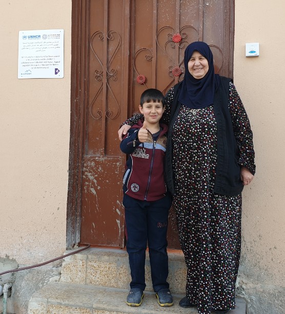 Ahkam and her grandson stand outside of their new home_Cash for Shelter
