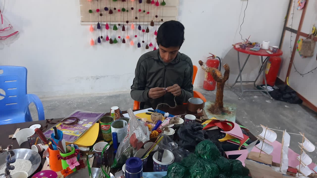 young man sitting a crafting table with supplies in front of him