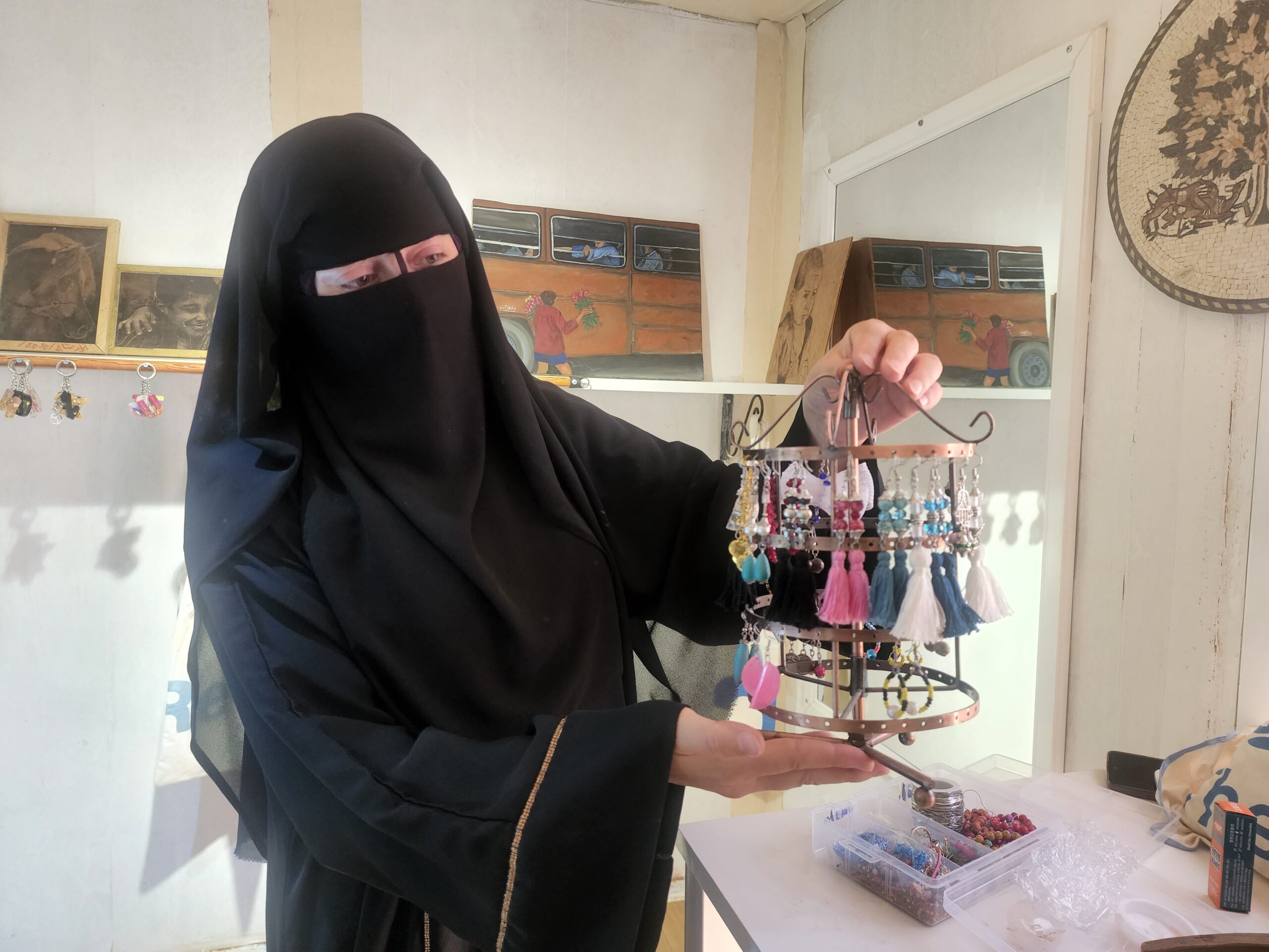 woman in hijab standing with the earrings she made at the made in za'atari center