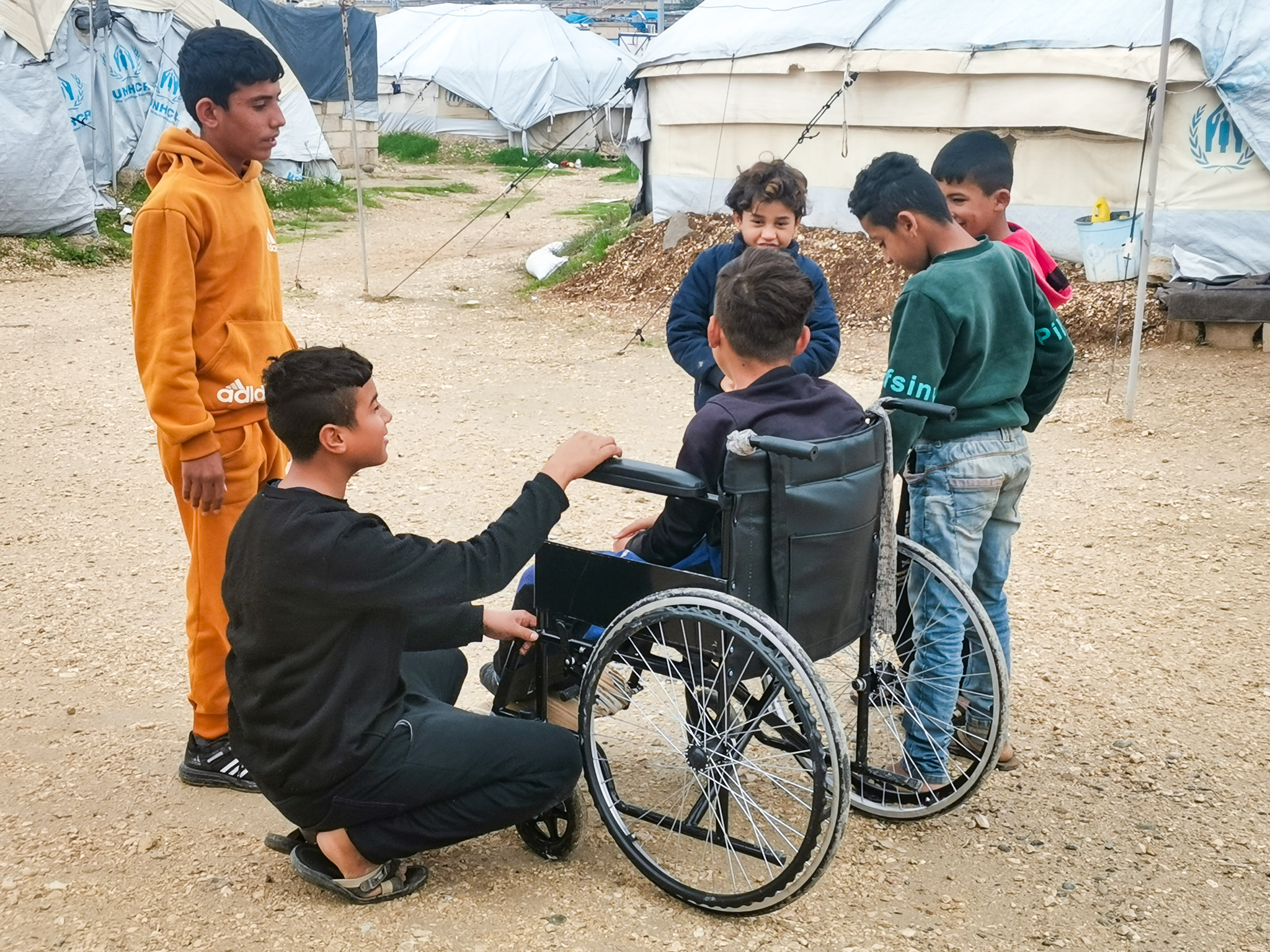 a boy in a wheelchair surrounded by other boys standing and looking at thim