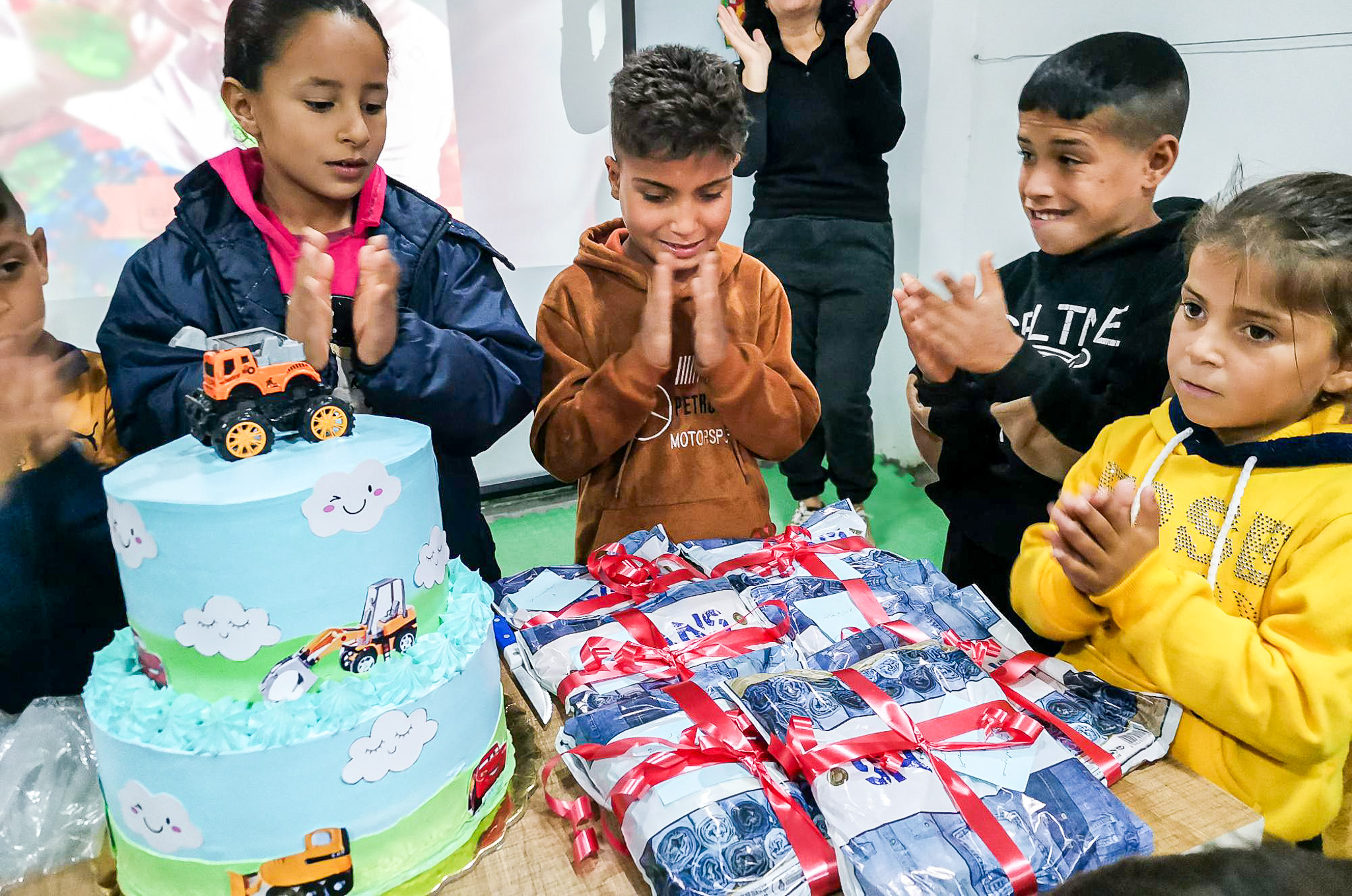 children stand around a table with a cake and gifts