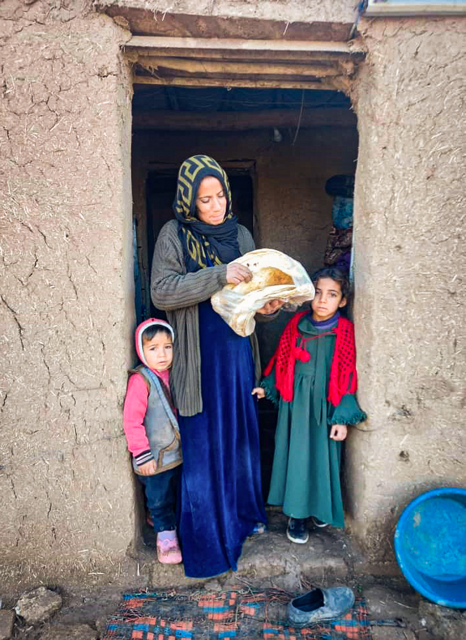 a woman in a hijab stands in a doorway with two children while holding bread