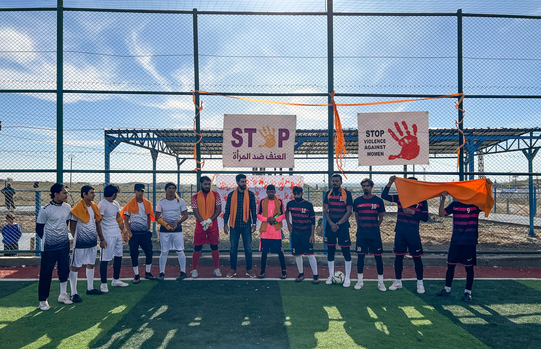 a group of young men stand on a soccer field under banners for preventing violence against women