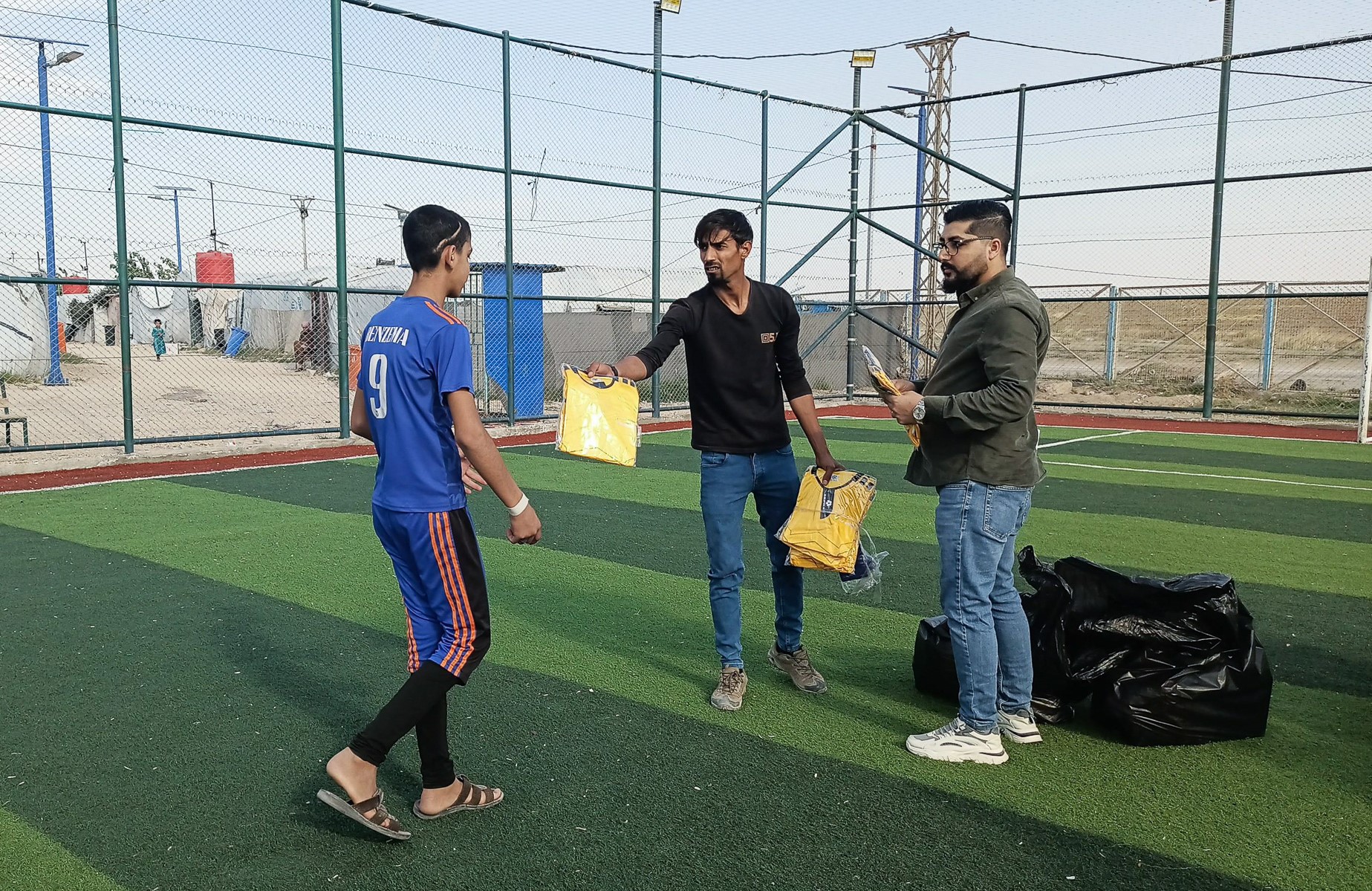 two men hand out soccer uniforms to a young man
