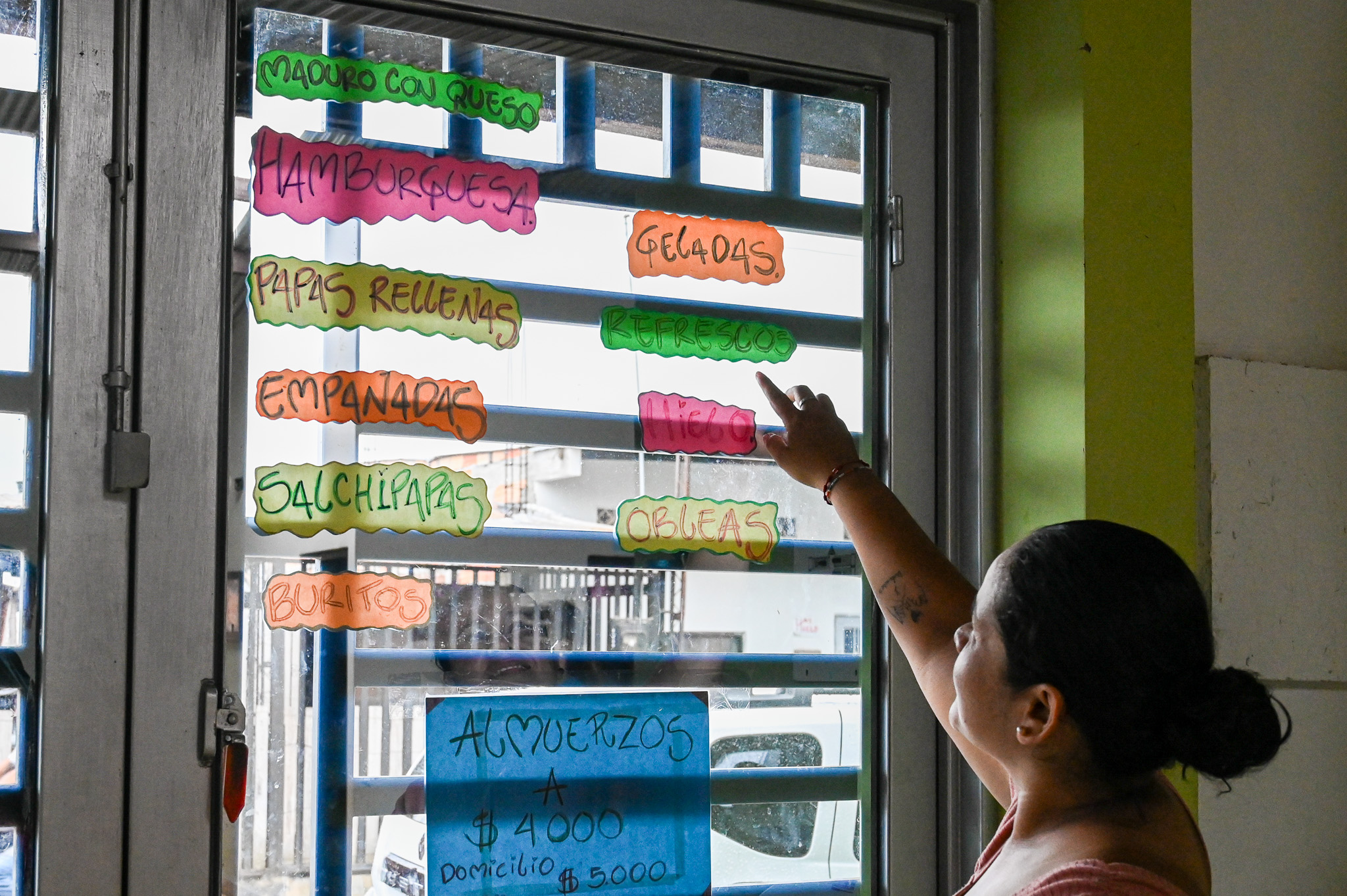 a woman stands with her back to the camera pointing at a colorful menu posted on her window