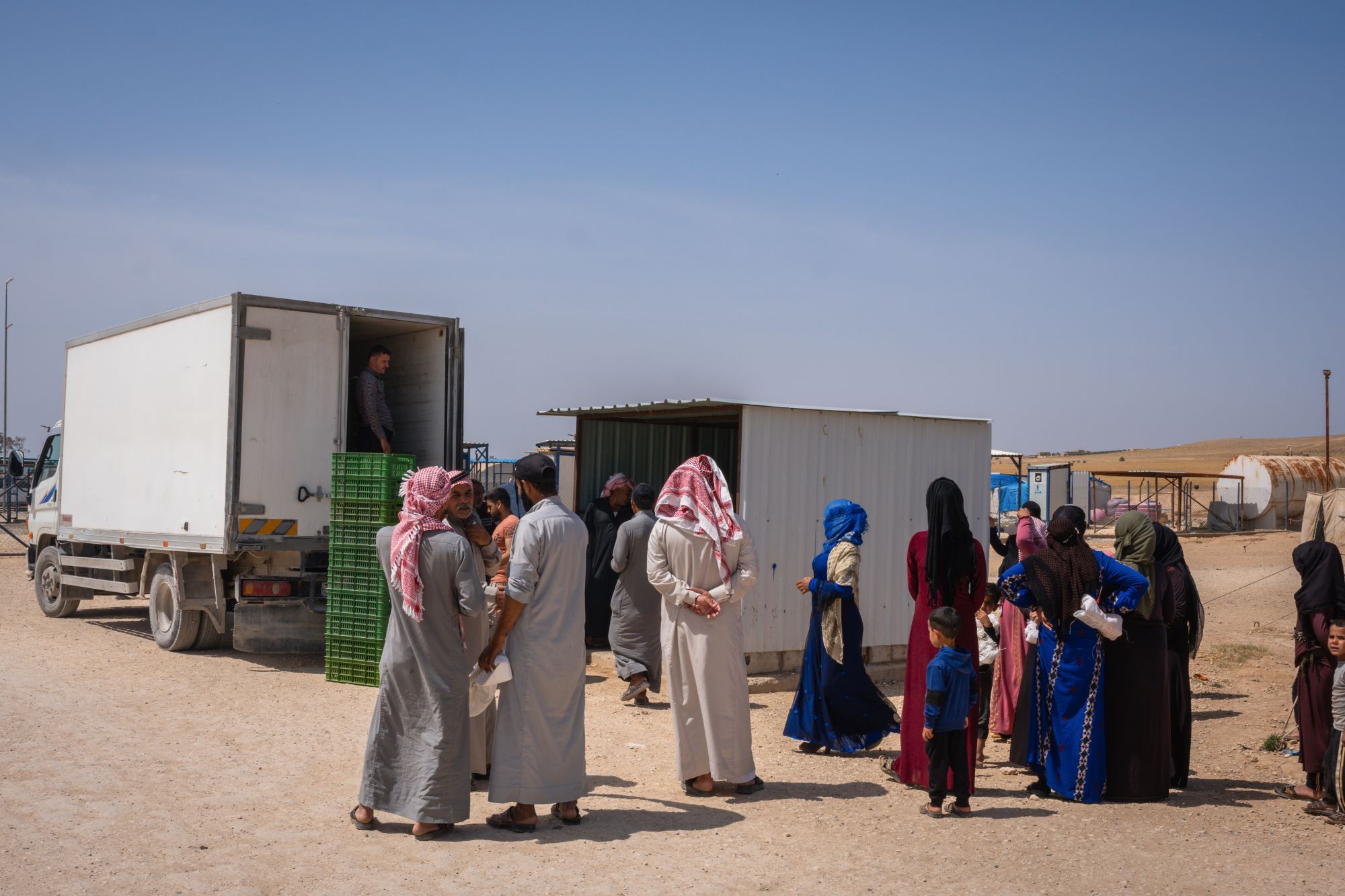 Syrian families line up at the back of a truck for bread distribution