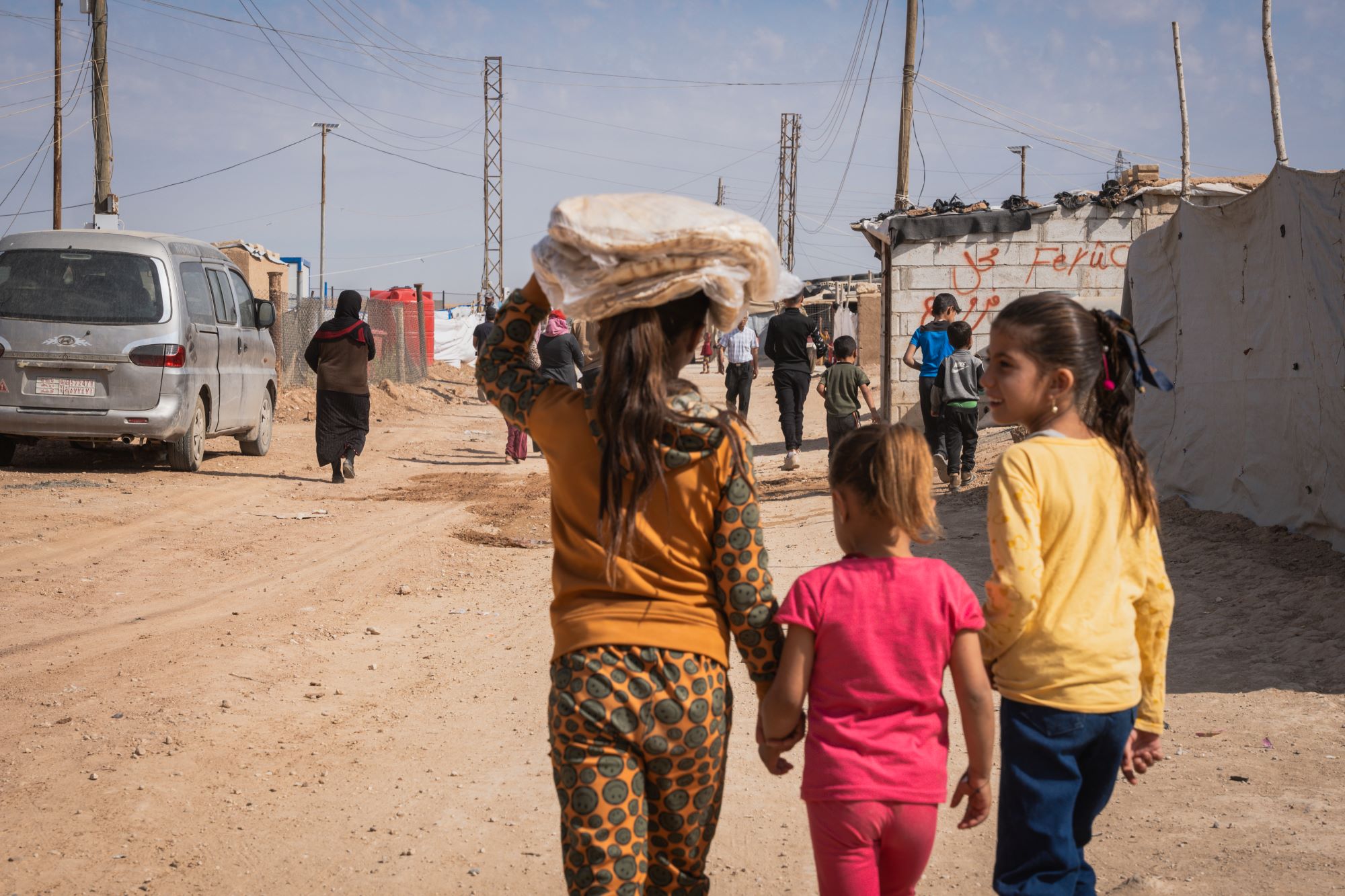 three girls walk down a dirt road with fresh bread in their hands