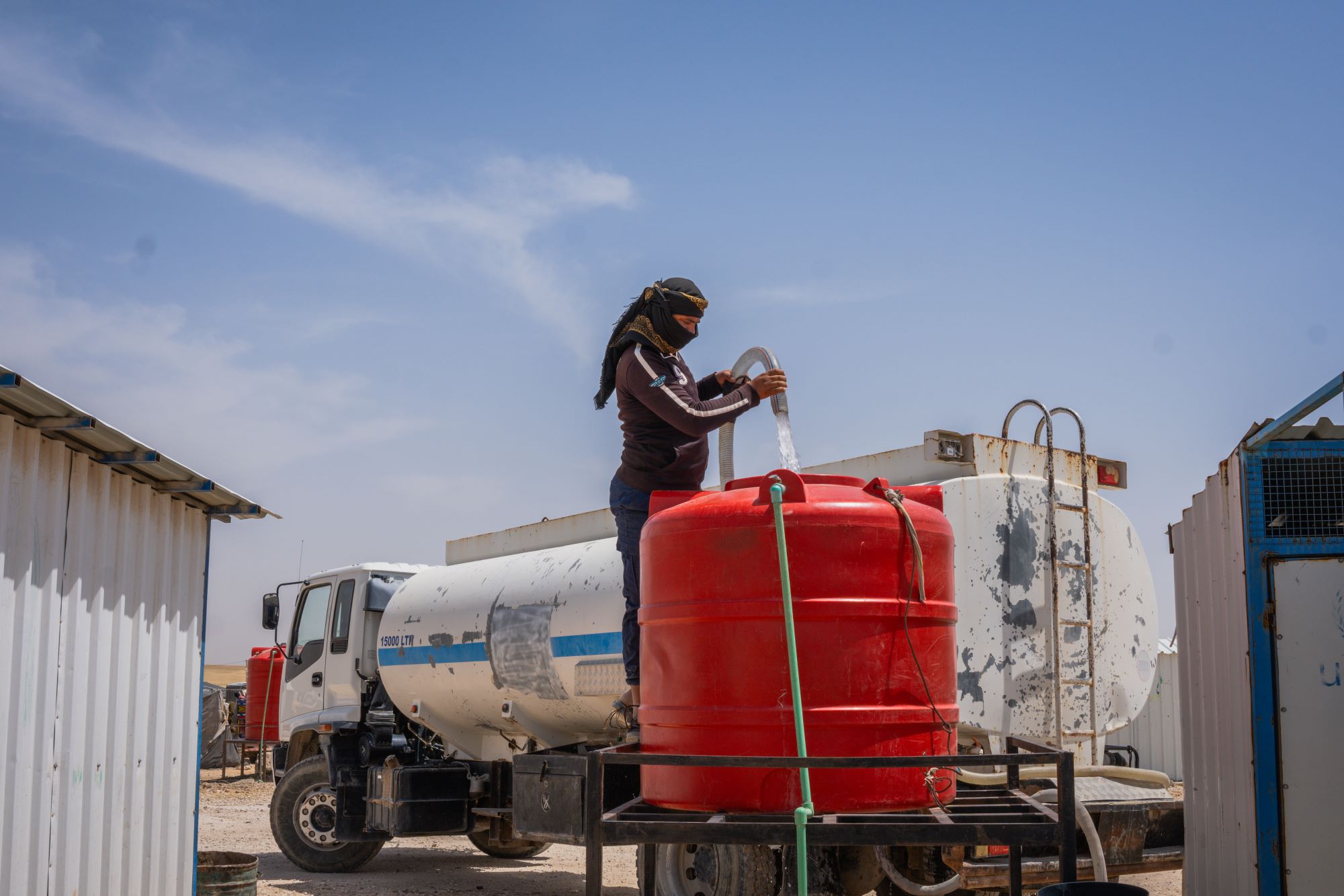 a humanitarian worker adds water from a truck into a water tank