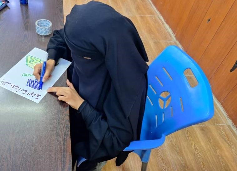 a woman wearing a niqab sits at a table drawing